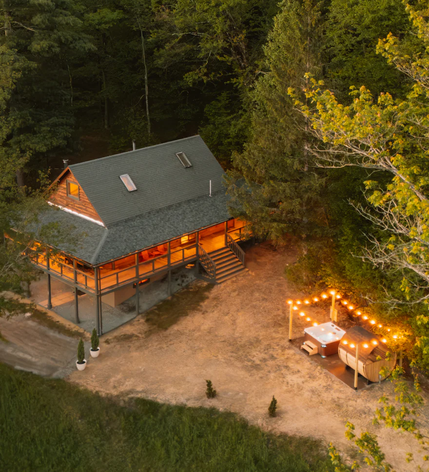 Forest cabin short-term rental lit up at dusk with outdoor dining